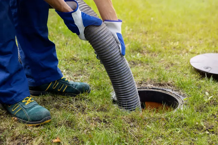 A man utilizes a hose to clear debris from a drain, ensuring proper drainage and cleanliness in the area.